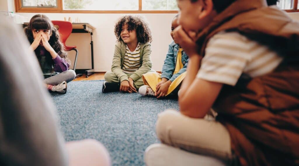 An elementary class gathers for their weekly classroom meeting on the carpet.