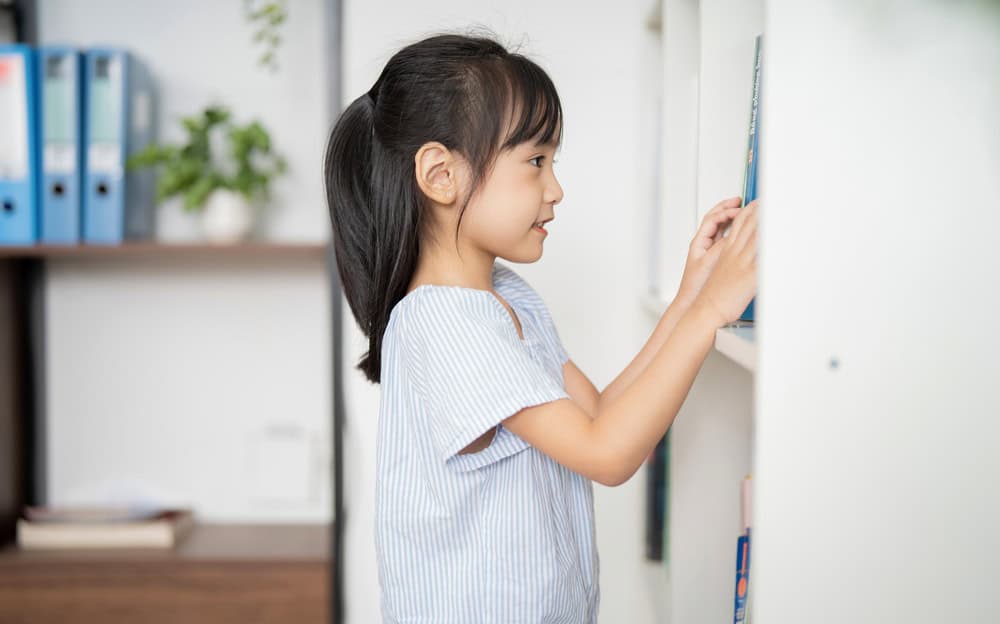 A young girl searching the shelves of her classroom for nouns as she plays a parts of speech game.