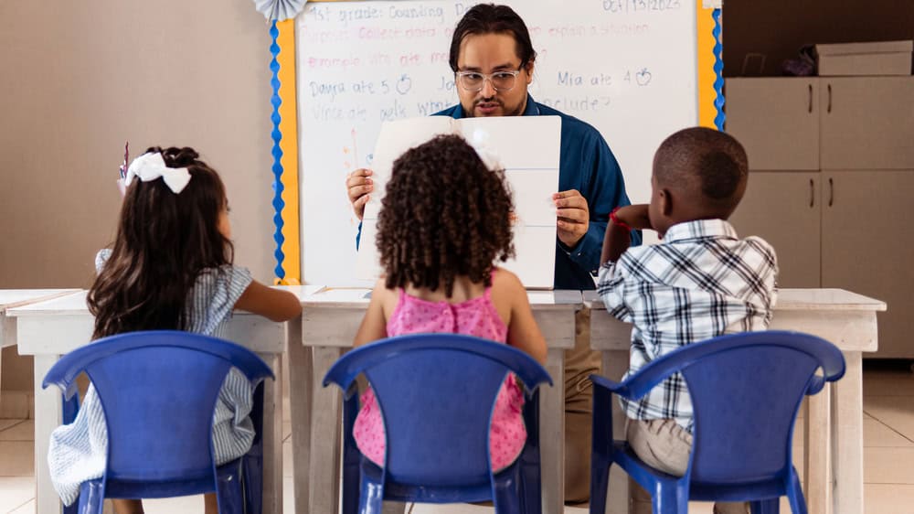 Male teacher holding a flashcard in front of 3 students for an exciting parts of speech activity.