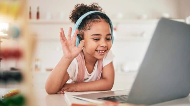 A picture of a young girl with headphones on sitting in front of her computer. excited to be signed up for Outschool classes.
