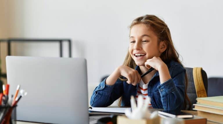 A picture of a 12 year old girl sitting at a desk looking at her lap top as she takes an Outschool class.