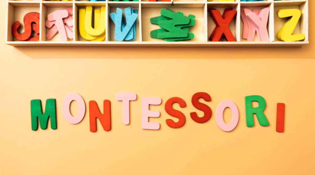The word MONTESSORI spelled out on an orange table in colourful felt letters next to a box of letters.
