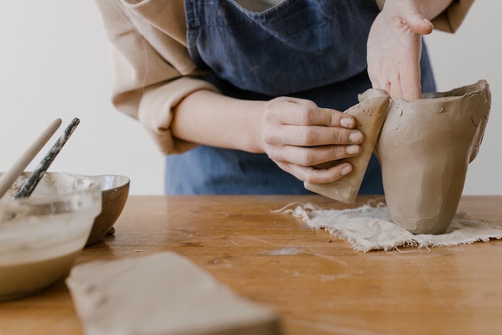 Close-up of hands shaping clay at a pottery worktable, showcasing the artistry of ceramics. A pottery kit is another excellent elementary graduation gift!