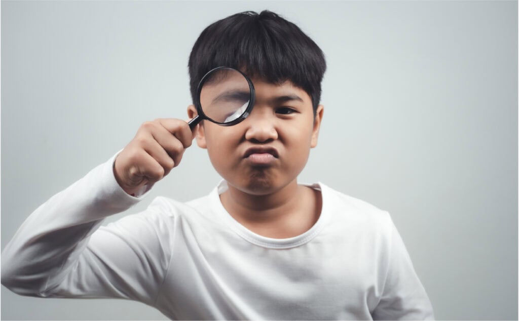An image of a 12 year old Asian boy holding a magnifying glass to his eye.