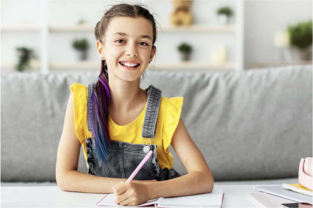 A 12 year old girl sitting at a desk holding a pencil.
