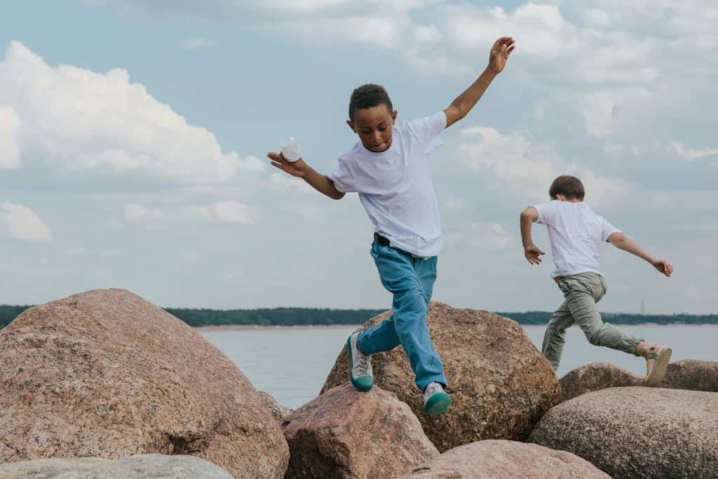 Two boys enjoy playing and climbing on seaside boulders on a clear day.
