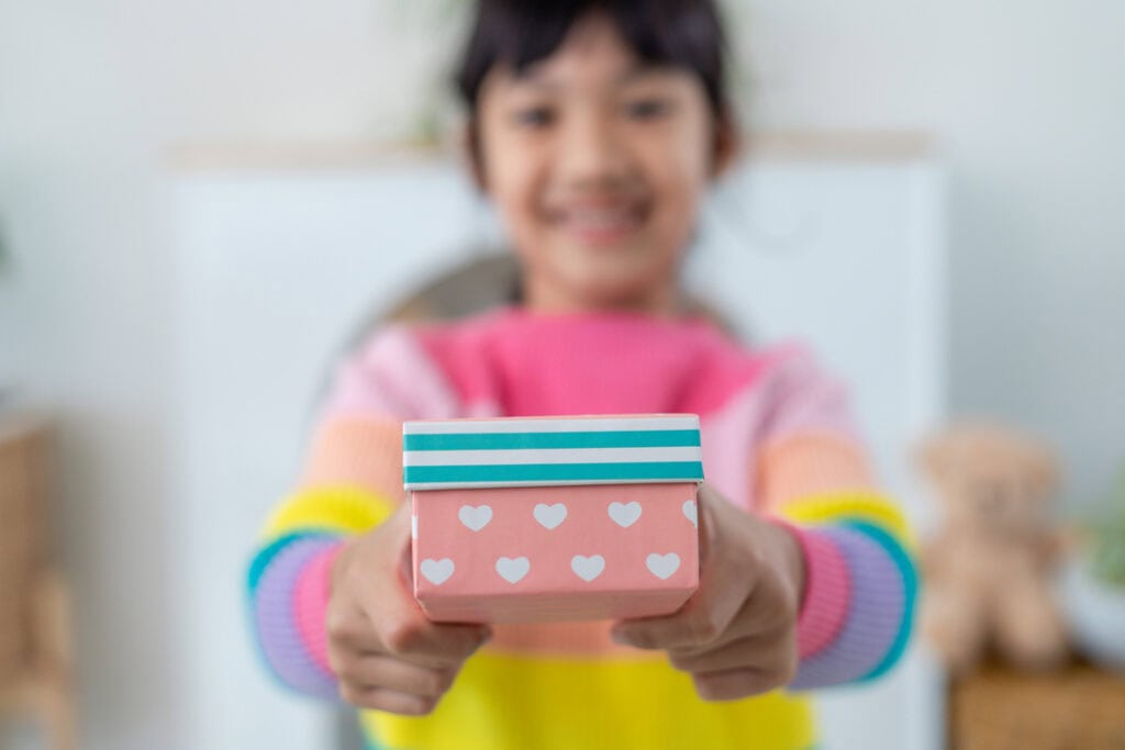 Little Asian girl smile and excited and holding red gift box in living room background. child holding gift box in Christmas and New year.Asian child girl smile and surprise.