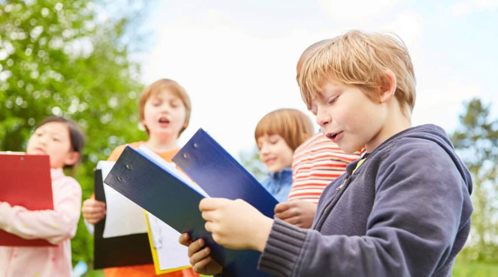 A small group of lower elementary students outdoors, each holding a clip board, getting ready to start an alphabet scavenger hunt