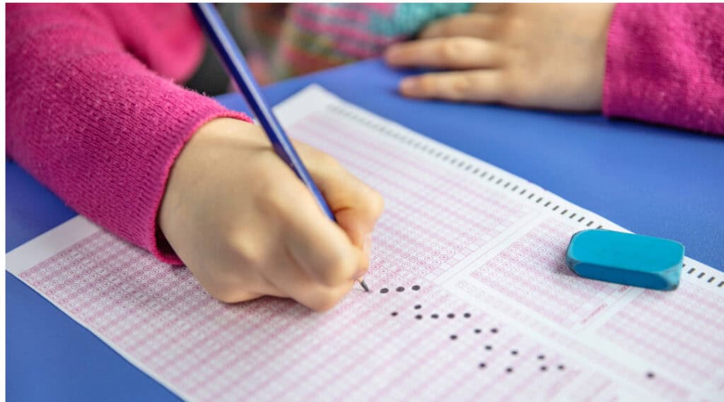 A photo of a young girls hands holding a pencil and filling in a test sheet. She is doing a standardized test.