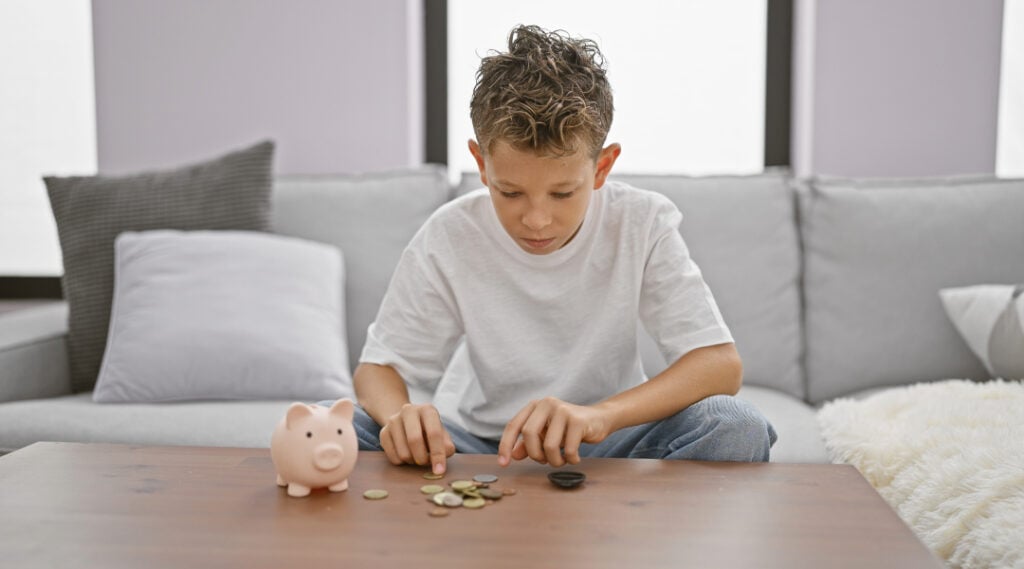 A young boy sitting at a table with a pile of coins in front of him. This is one of those summer math activities that kids love getting their hands on!