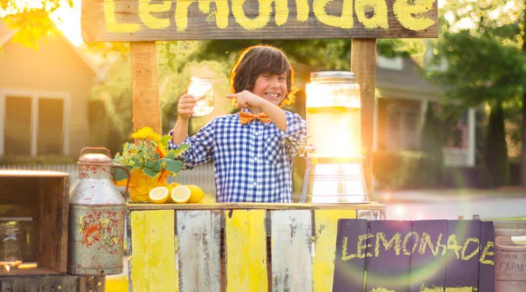 A young boy proudly standing at his lemonade stand.