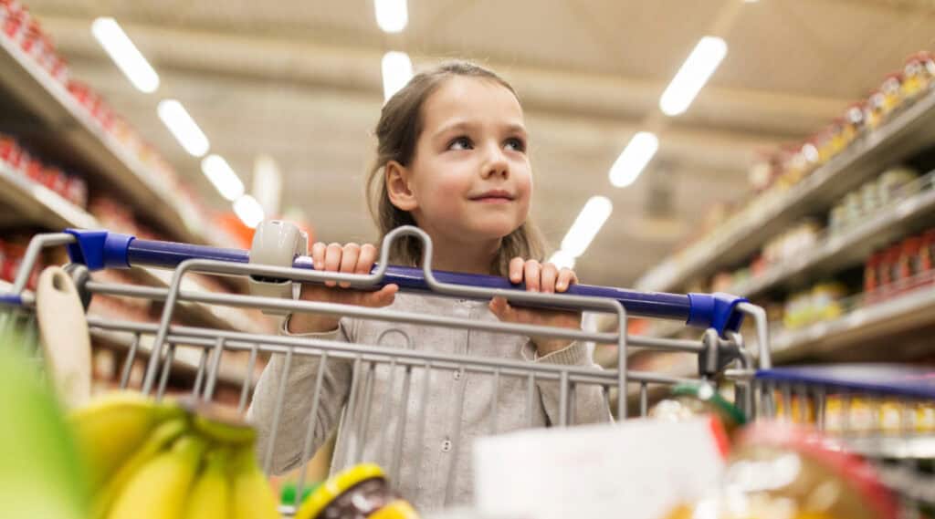 A young girl pushing a grocery cart at the supermarket. She's learning a lot through this simple summer math activity.
