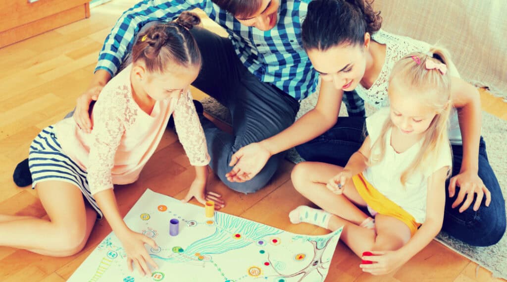 Two young girls showing their mom and dad the math board game they made together. This is a one of my favorite summer math activities.