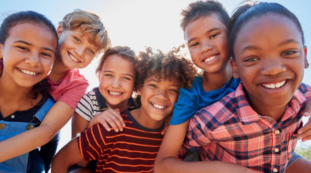 a group of children smiling and looking at the camera. They're excited to try some summer math activities.