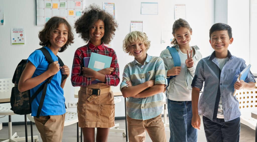 A picture of 5 students standing in a classroom smiling at the camera. These are Montessori students who have transitioned successfully to a traditional middle school.