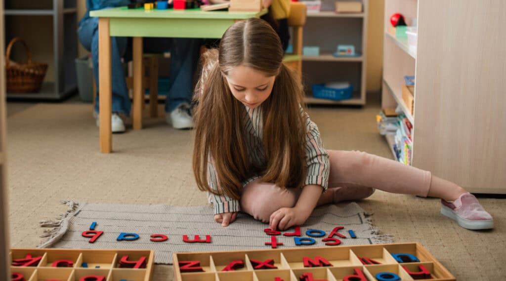 A girlworking with the moveable alphabet while sitting on the floor in a Montessori classroom.
