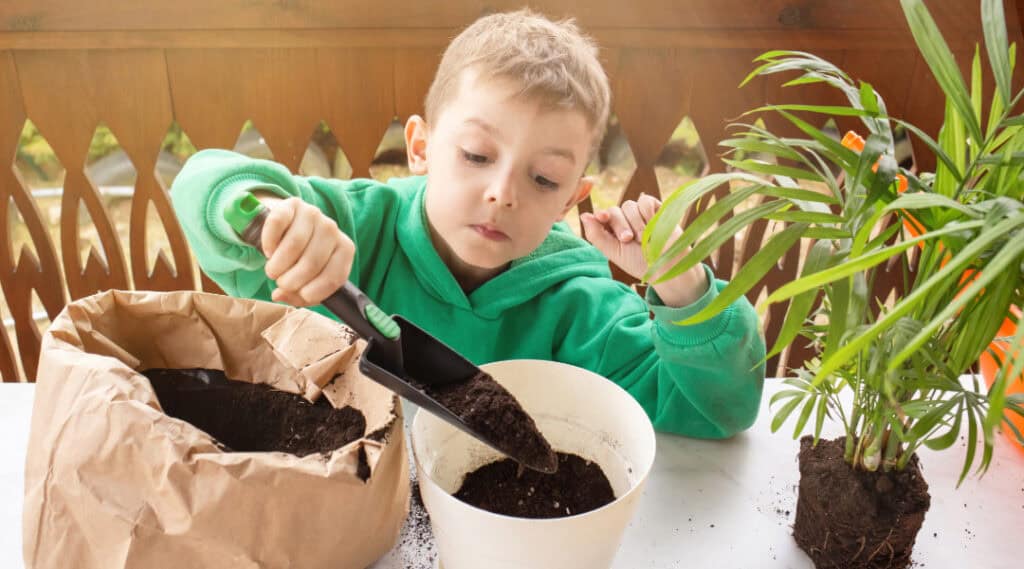 A young boy pouring soil into a planter.