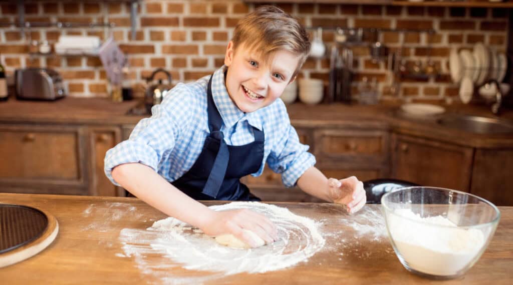 A young boy kneading dough and baking something as part of a summer math activity at home.