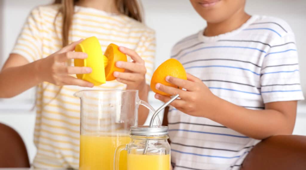 A boy and a girl and squeezing lemons to make lemonade for their small business of selling lemonade.