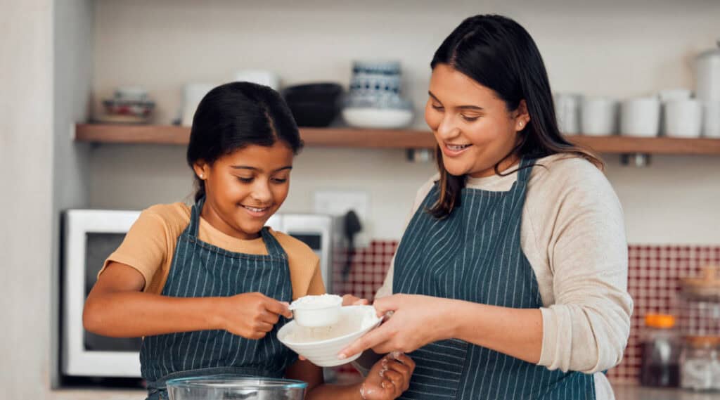 A mother and daughter engaging in some summer math activities in the kitchen as they measure and bake together.