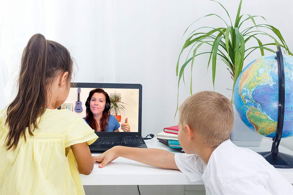 Two students working at laptop with a fun Outschool Teacher smiling back at them