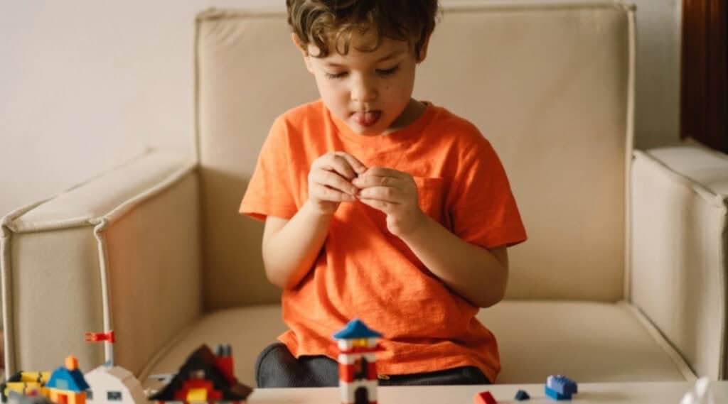 There are many virtual summer camps for Lego lovers. Here a young boy concentrates as he builds with Lego.