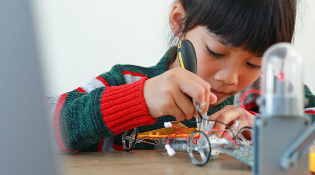 A young girl is using tools to build a small car.