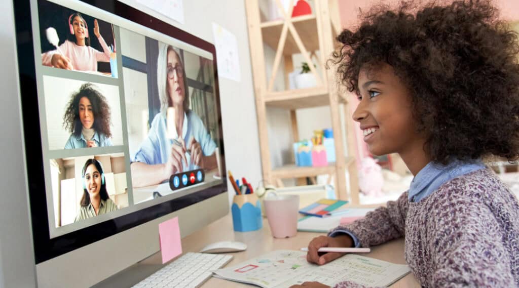 A young girl taking an online class. you can see the teacher and three other students on her laptop. One of the many benefits of Outschool is that you can take classes anywhere!