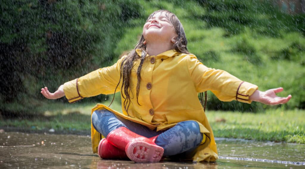 Happy young girl sitting in the rain.