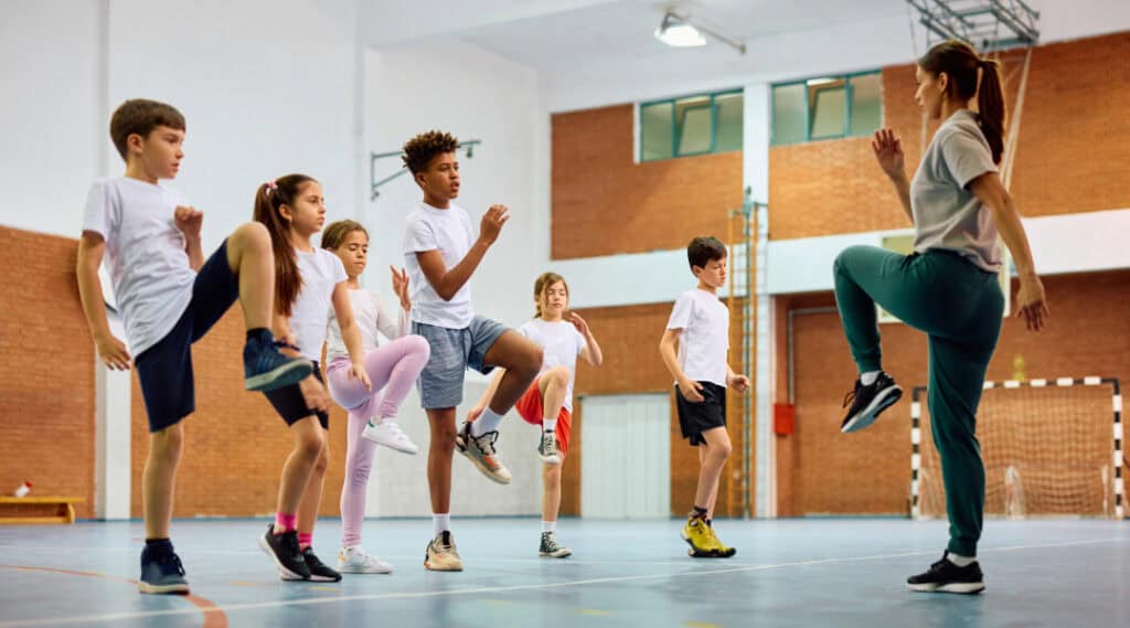 A picture of gym class with a teacher leading movements in the gymnasium.