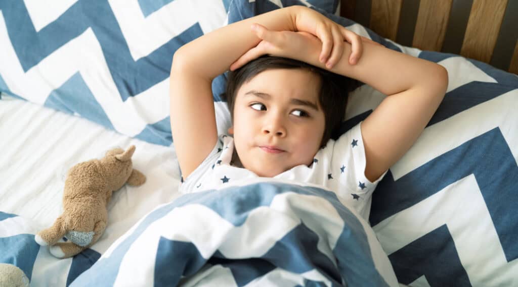 An image of a grade 1 boy in his pajamas laying in bed, ready to sleep. An excellent back to school tip for families is to get kids to bed earlier.