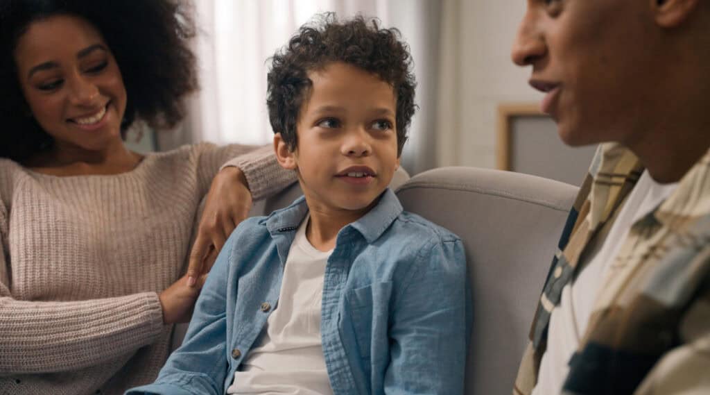 A 7 year old boy sitting on the couch with his mom and dad having a conversation.