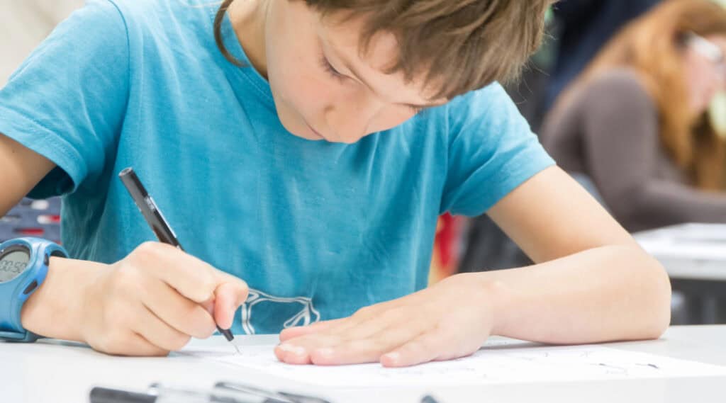A young boy is focused using a black pen to do some art.