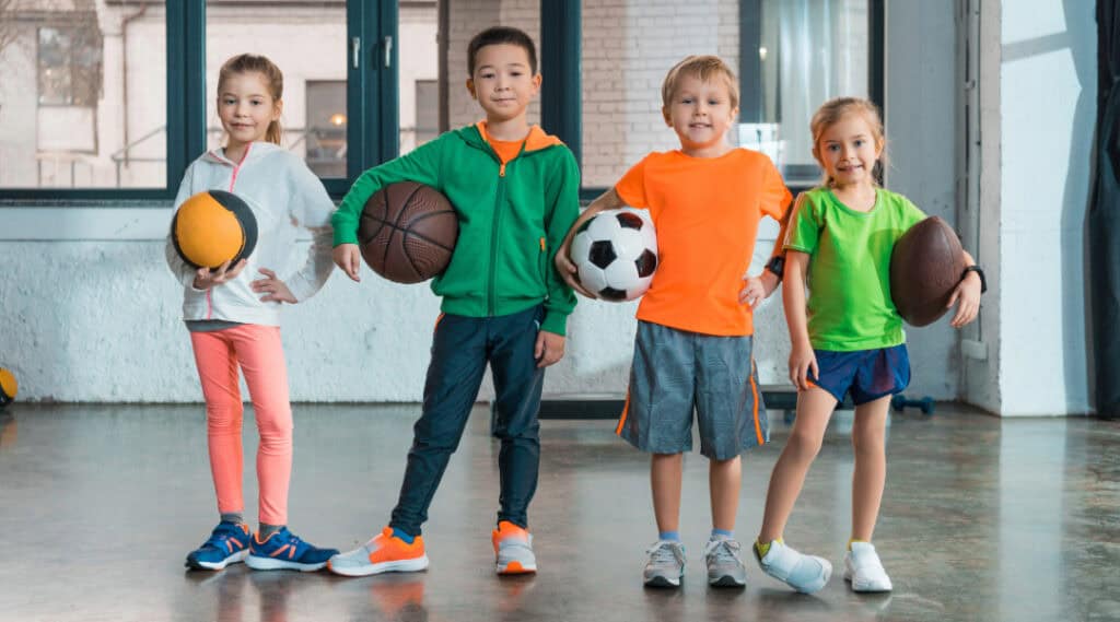 Don't forget to add comfy clothes to your back to school supplies list! Here's a picture of 4 young students in cofy clothes, each holding a different sports ball.