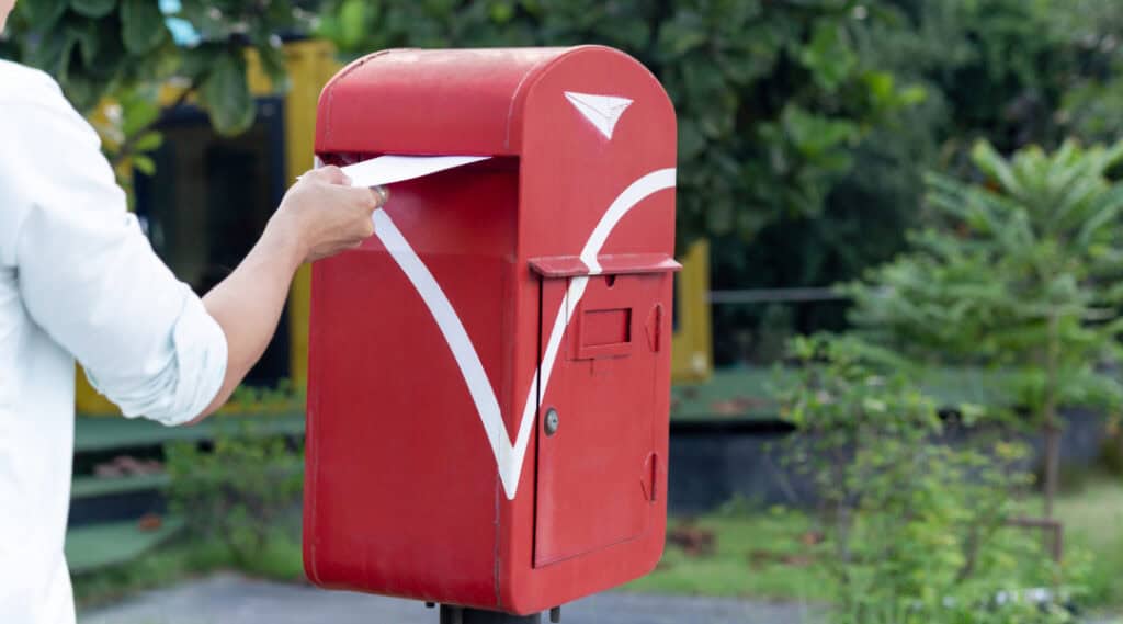 A picture of a mailbox and a woman putting a card in the mailbox. Advice from a teacher is to send students a card during the summer months.
