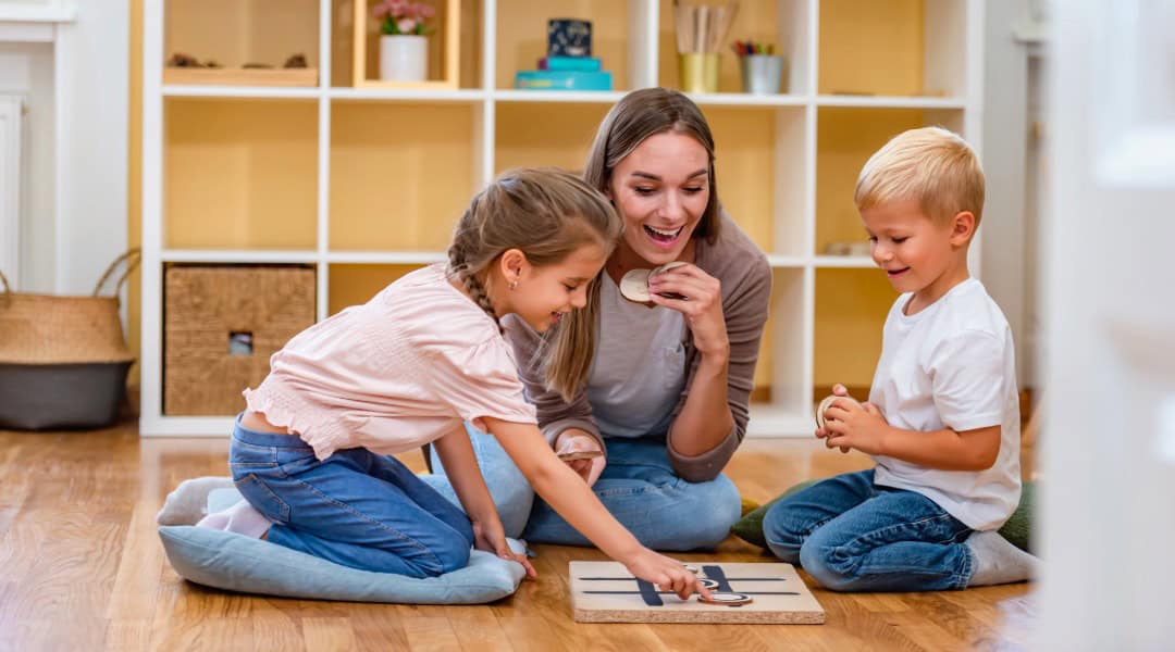 A teacher sitting on the floor with a young boy and girl who are playing tic tac toe with parts of speech. Such a fun way to build knowledge.