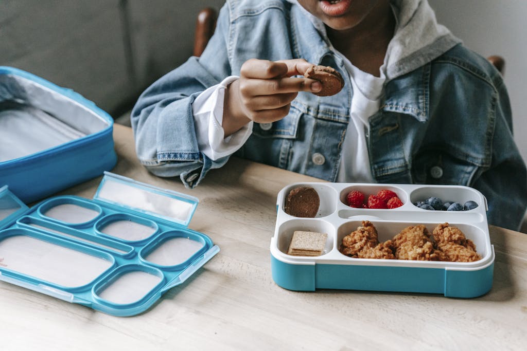 A young boy enjoys a healthy and tasty lunch box meal with fresh fruits and cookies. Be sure to put a solid, reuseable lunch box on your kids' back to school supplies list.