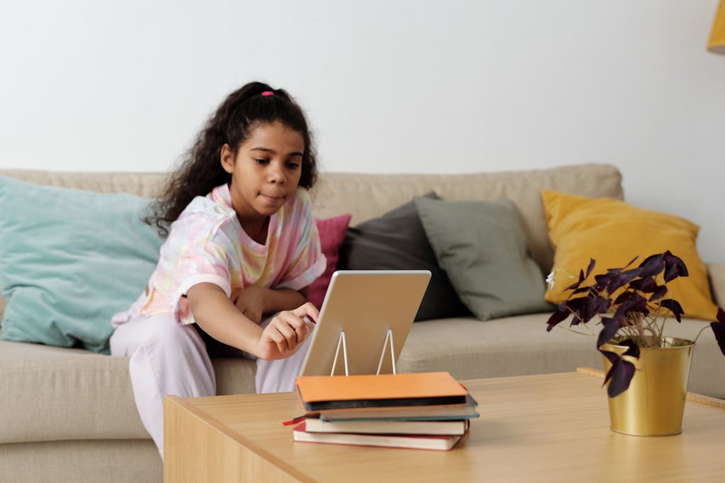 A young girl using a tablet for online learning at home, sitting comfortably on a couch.