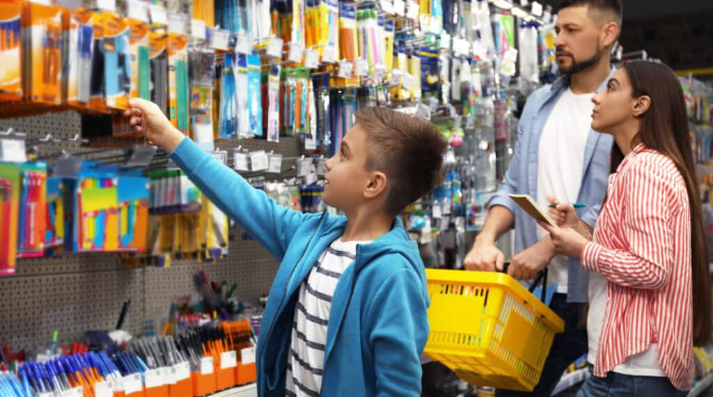 A picture of a young boy selecting back to school supplies in a store with his mom and dad.