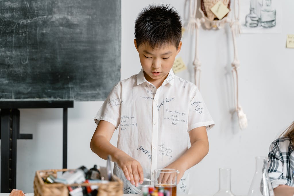 Boy in a classroom conducting a science experiment, wearing a white shirt. He's using one of the subscription boxes for kids his teacher signed the class up for.