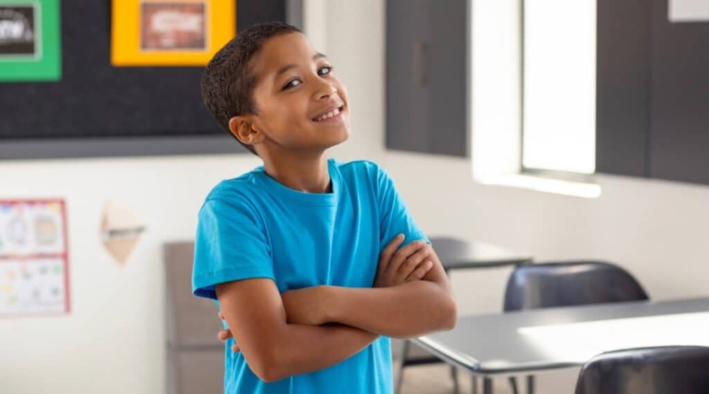A young boy in a blue shirt sitting with arms crossed in the classroom.