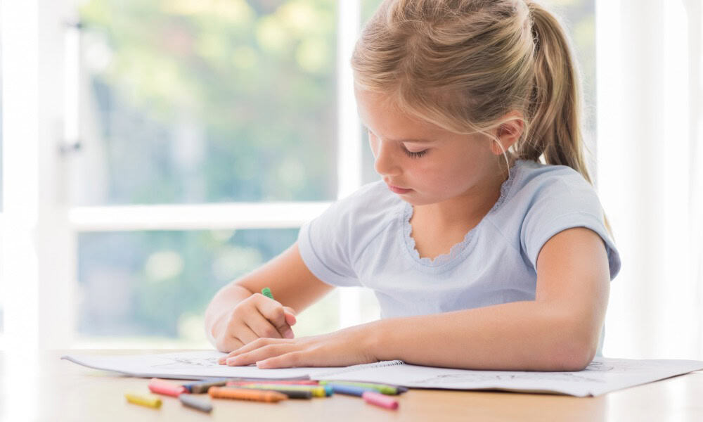 A picture of a young girl at a table coloring our cat facts coloring book.
