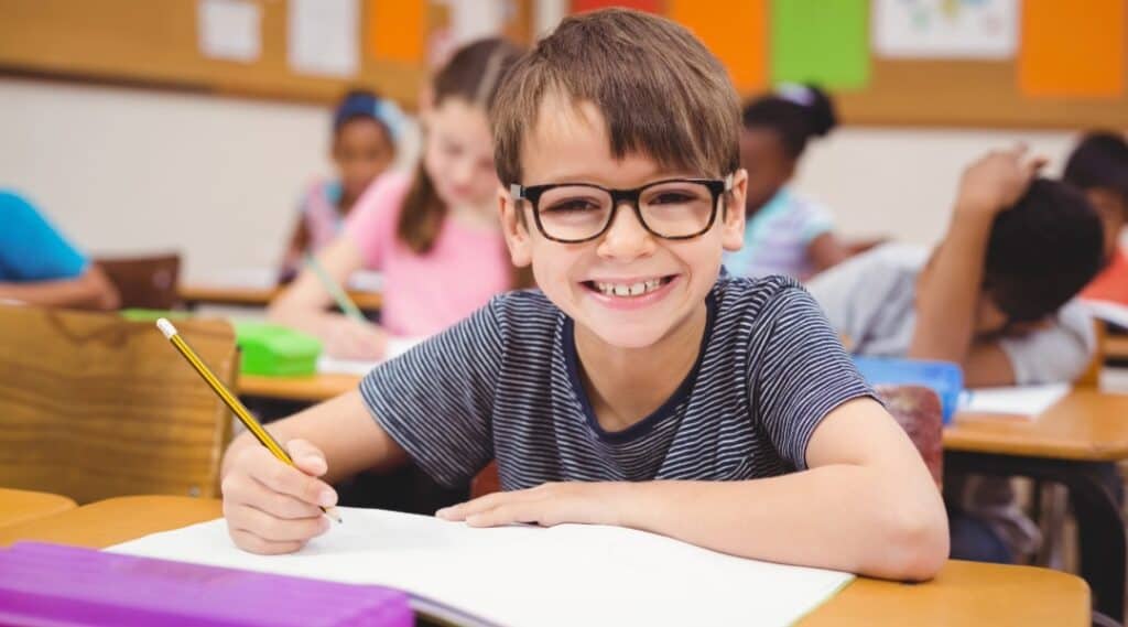 A smiley young boy sitting at a desk writing in his journal about a Charlie Kirk quote.