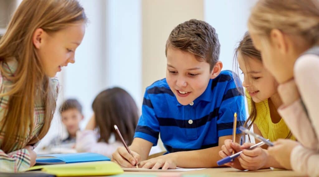 Three elementary aged students word together to learn grammar using parts of speech charts