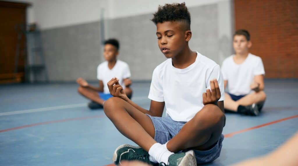 A young boy sits cross legged with his eyes closed.