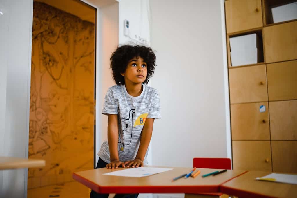 A young child stands attentively by a desk in a colorful and engaging classroom.