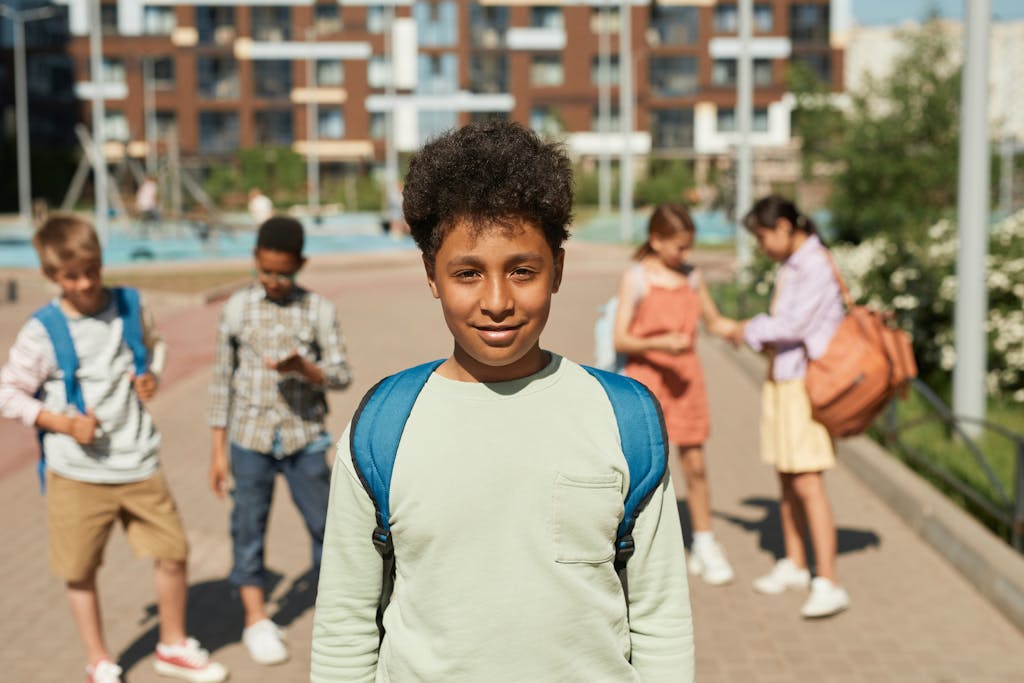 Group of children happily returning to school on a sunny day, carrying backpacks and smiling.