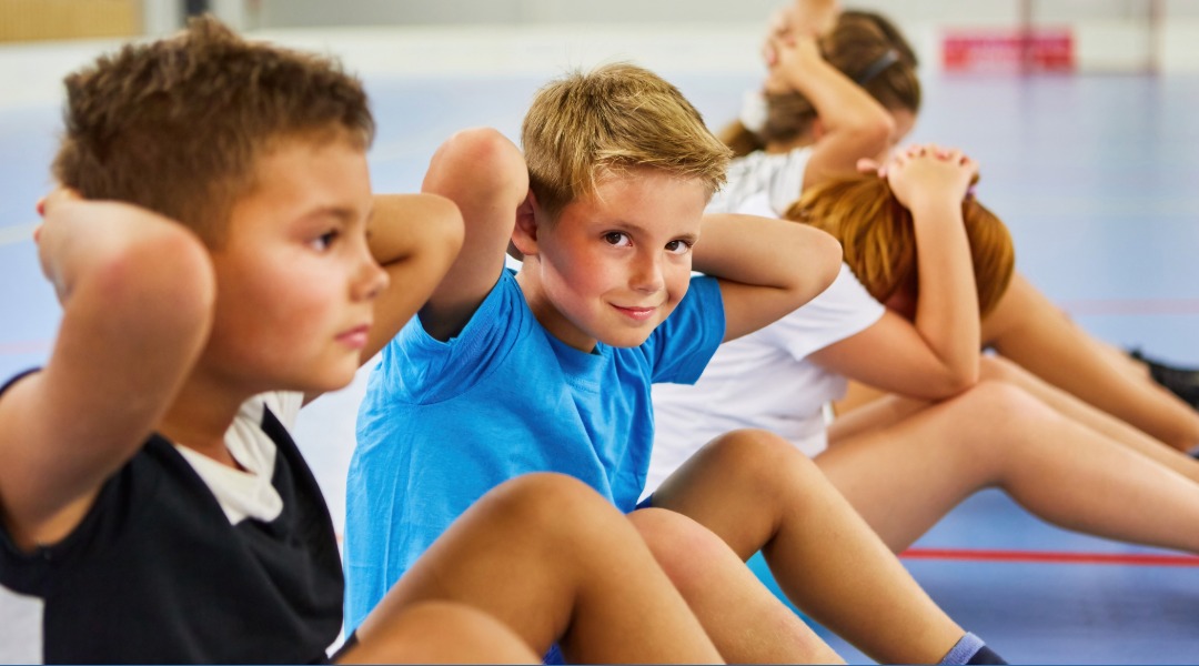 An elementary class doing sit ups as part of their 100th day of school activities and celebrations.