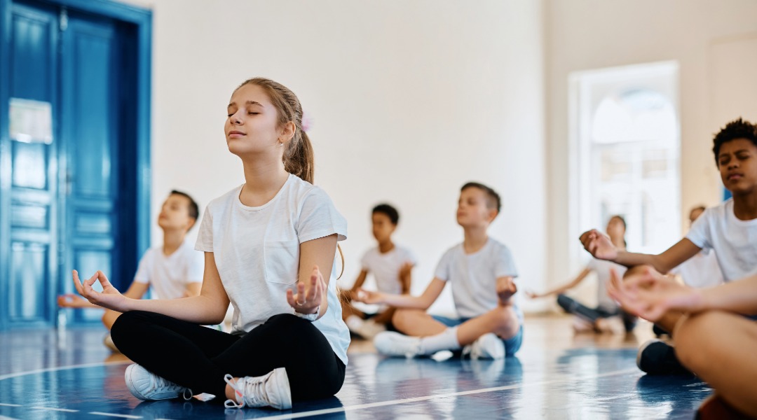 A class meditating on the gym floor as part of their 100th day of school activity where they remain silent for 100 seconds.