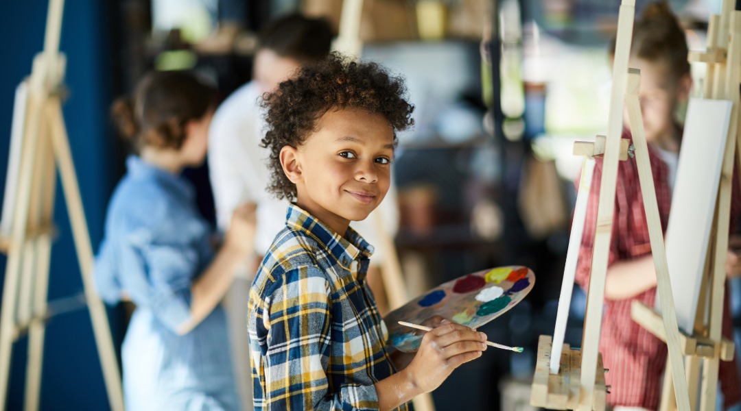 A young boy standing at an easel ready to paint a portrait of his 100 year self.